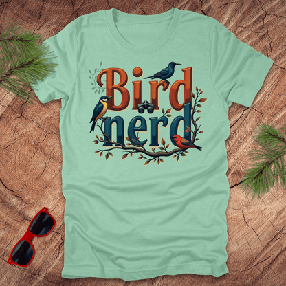 A heather mint t-shirt with a graphic print of birds and the text 'Bird nerd', surrounded by foliage and a pair of binoculars lying next to it on a wooden surface.