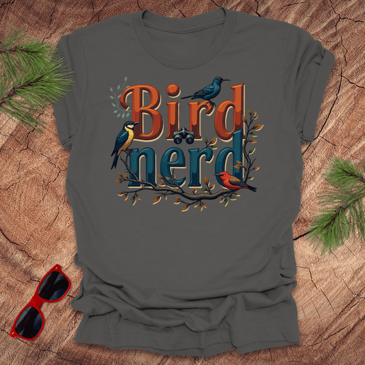 An asphalt-shirt with a graphic print of birds and the text 'Bird nerd', surrounded by foliage and a pair of binoculars lying next to it on a wooden surface.