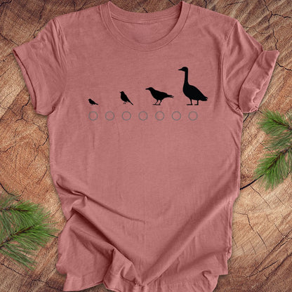 Mauve t-shirt with black bird illustrations on a wooden surface