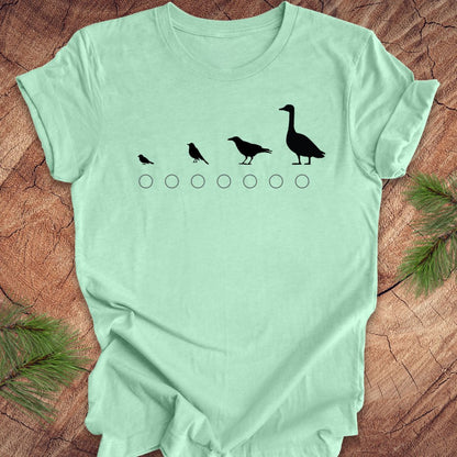 Light green t-shirt with black bird graphic on a wooden surface