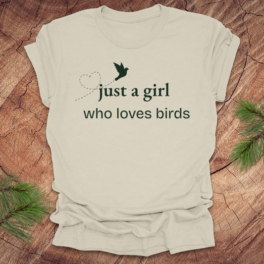 Beige t-shirt with 'just a girl who loves birds' text and bird graphic on a wooden surface.