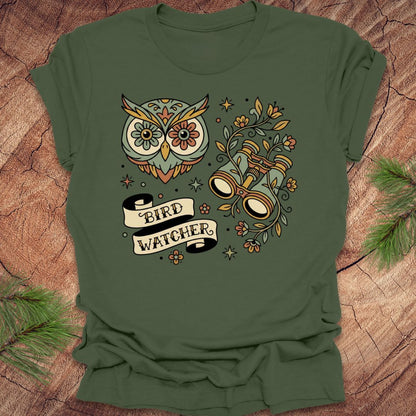 Green t-shirt with owl and binoculars design, with text 'bird watcher' on a wooden surface