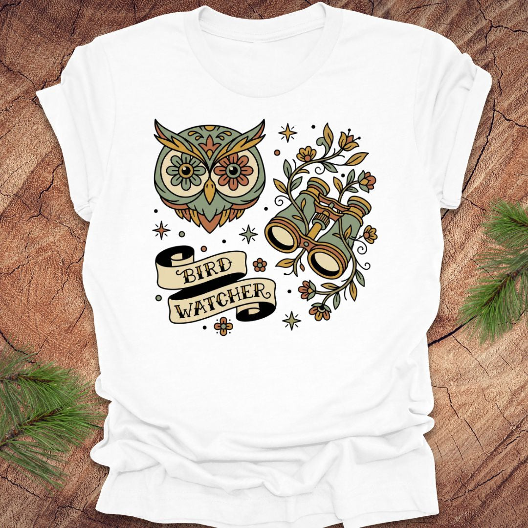 White t-shirt with owl and binoculars design, with text 'bird watcher' on a wooden surface