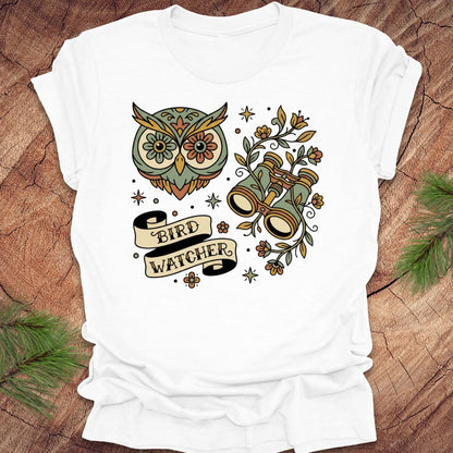 White t-shirt with owl and binoculars design, with text 'bird watcher' on a wooden surface