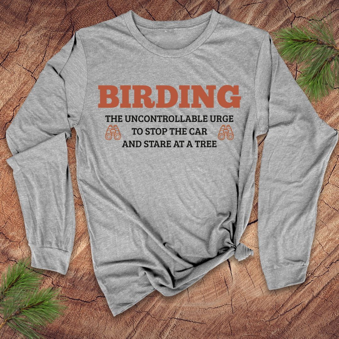 Gray long-sleeve shirt with humorous birding text on a wooden surface with pine branches.