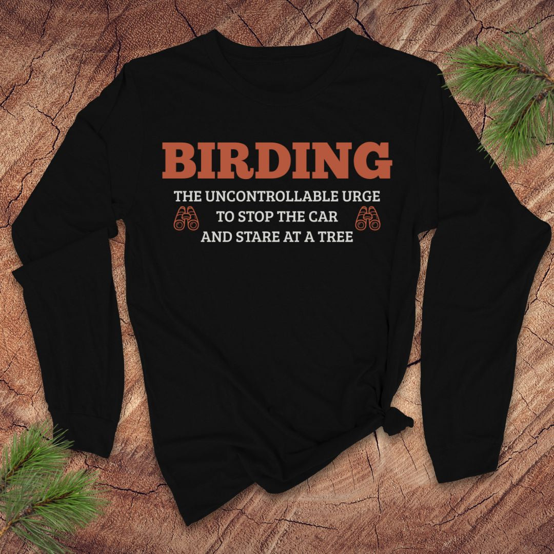 Black long sleeve tshirt with funny 'BIRDING' text on a wooden surface with pine branches.