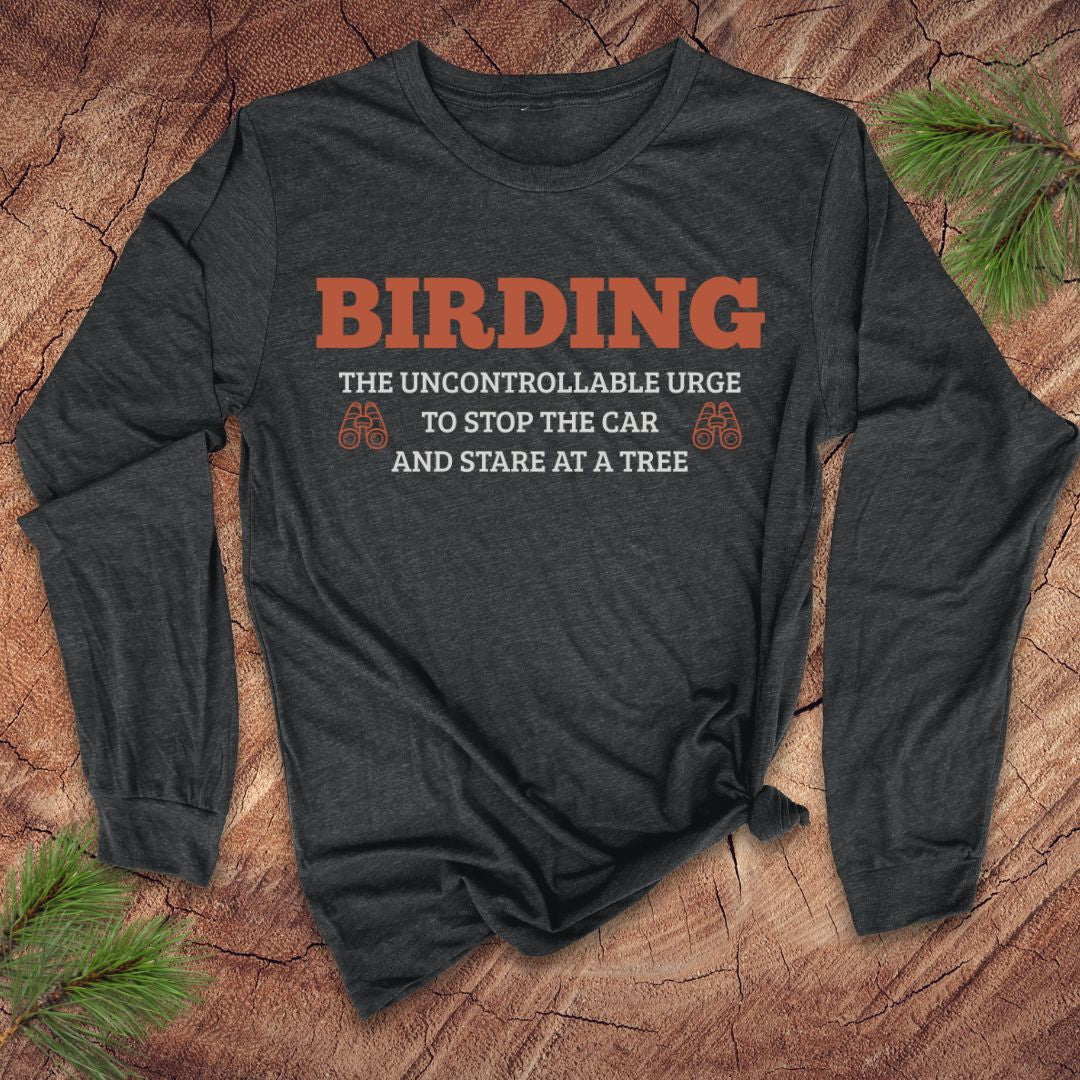 Dark gray long-sleeve shirt with funny 'BIRDING' text on a wooden surface with pine branches.