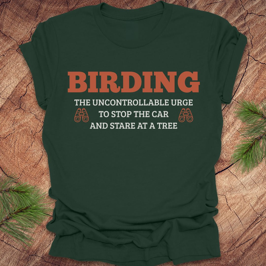 Green t-shirt with 'BIRDING' text on a wooden surface with pine branches.