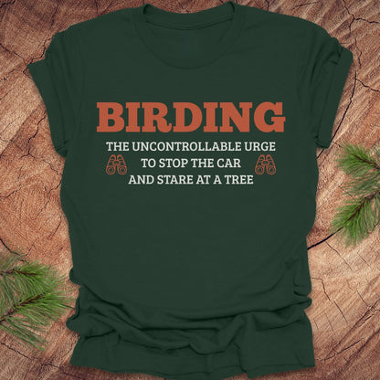 Green t-shirt with 'BIRDING' text on a wooden surface with pine branches.