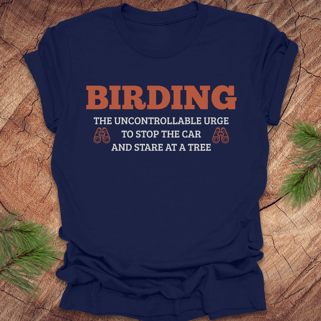 Navy blue t-shirt with 'BIRDING' text on a wooden surface with pine branches.