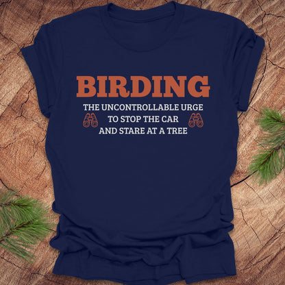 Navy blue t-shirt with 'BIRDING' text on a wooden surface with pine branches.