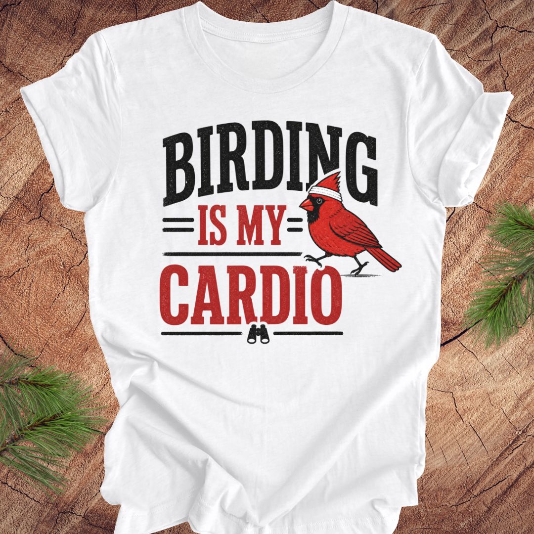 White t-shirt with 'BIRDING IS MY CARDIO' text and cardinal graphic on a wooden surface.