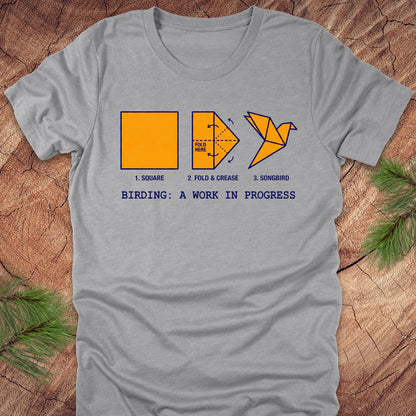 Gray t-shirt with origami bird design and text on a wooden surface