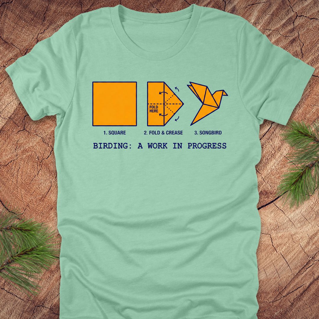 Light green t-shirt with origami bird design and text on a wooden surface