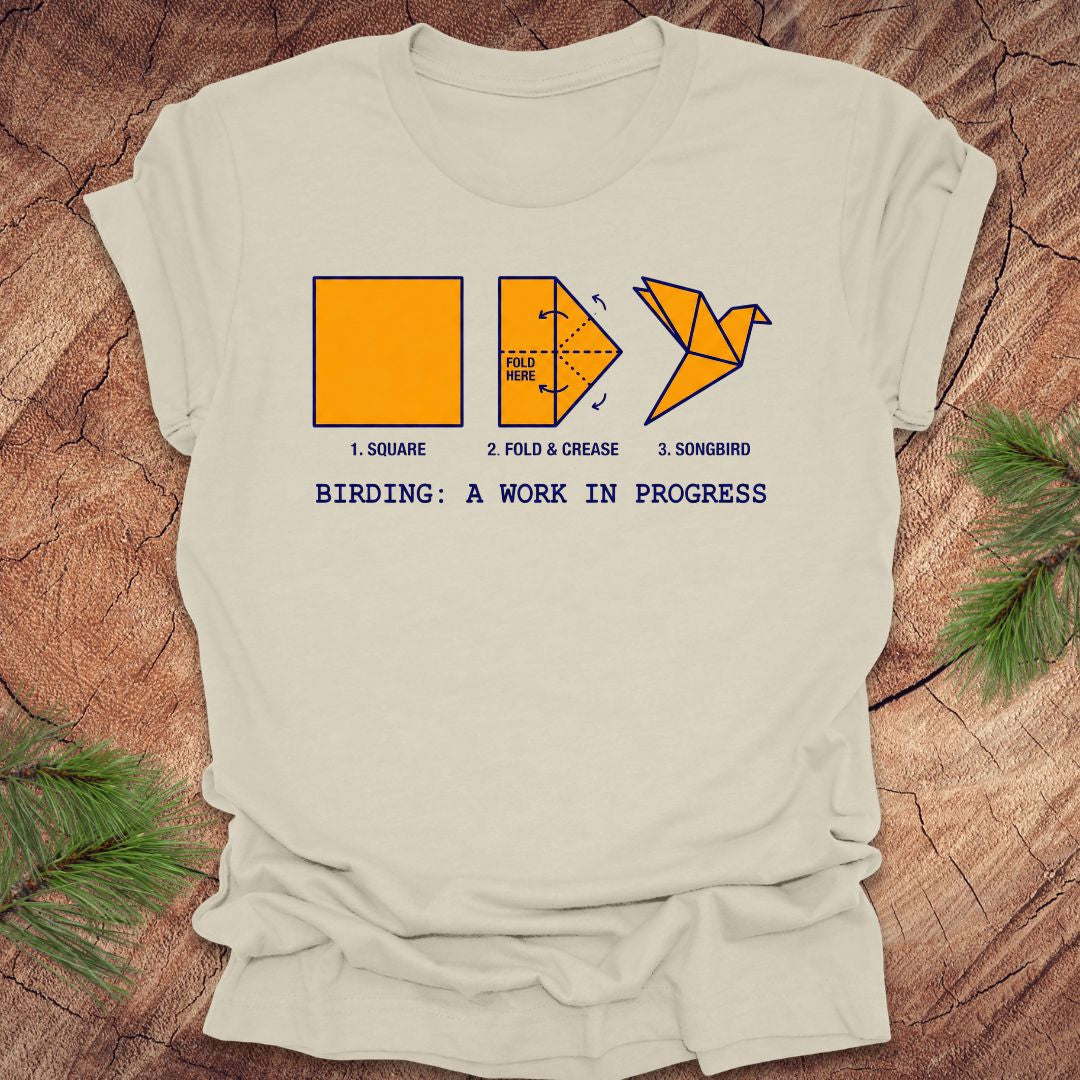 Beige t-shirt with origami bird design and text on a wooden surface