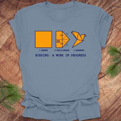 Blue t-shirt with origami bird design and text on a wooden surface