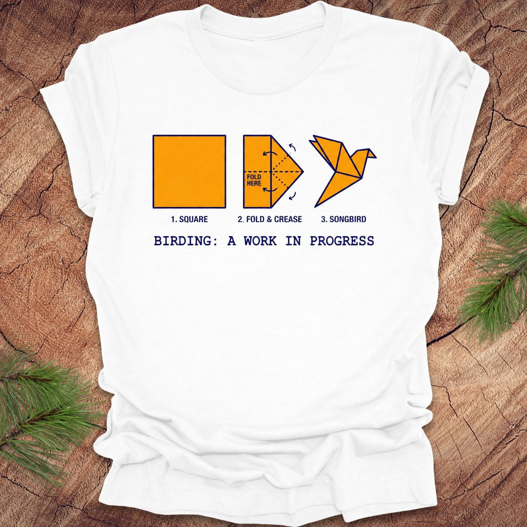 White t-shirt with origami bird design and text on a wooden surface