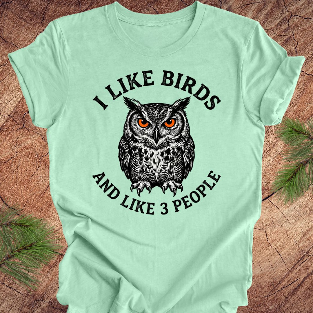 Light green t-shirt with an owl graphic and text on a wooden surface.