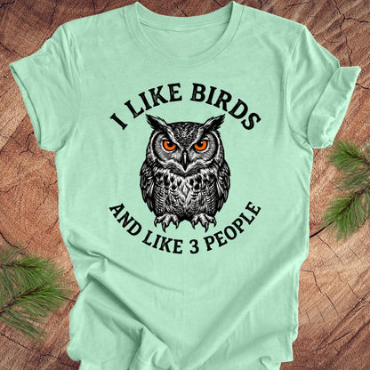 Light green t-shirt with an owl graphic and text on a wooden surface.
