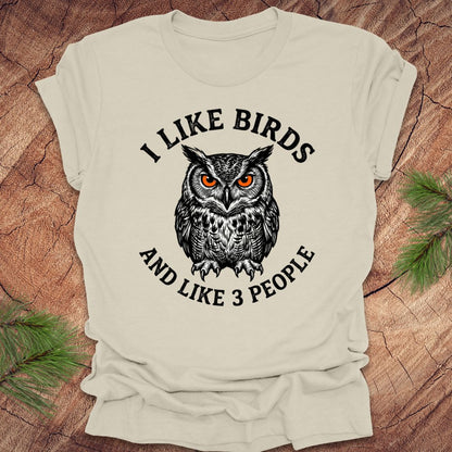 Beige t-shirt with an owl graphic and text, 'i like birds and like 3 people' on a wooden surface