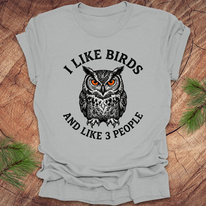Silver t-shirt with an owl graphic and text, 'i like birds and like 3 people' on a wooden surface