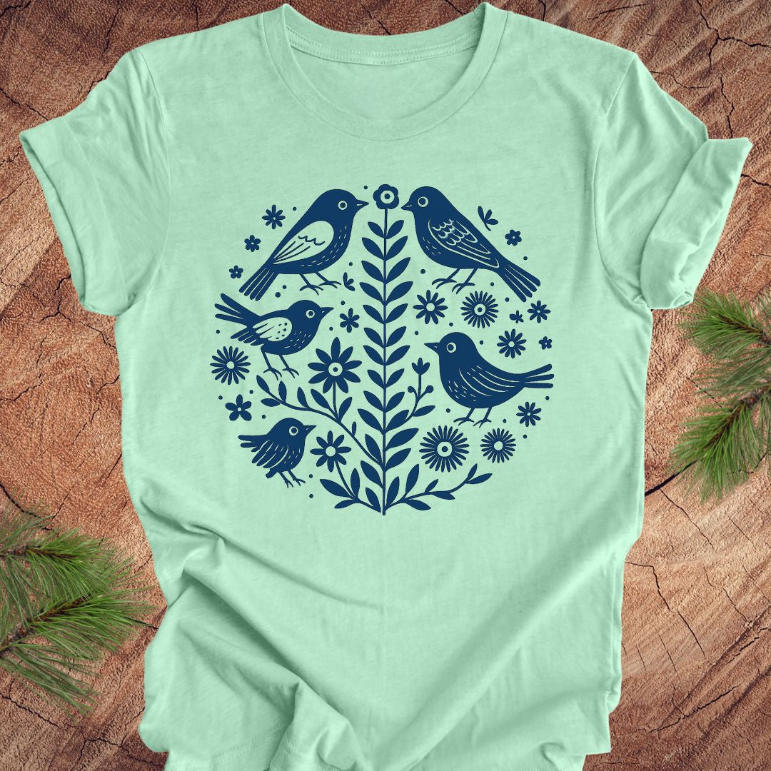 Mint green t-shirt with folk art blue bird and floral design on a wooden surface