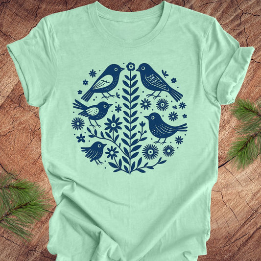 Mint green t-shirt with folk art blue bird and floral design on a wooden surface