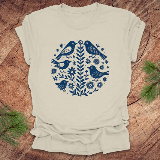 Beige t-shirt with folk art blue bird and floral design on a wooden surface