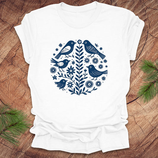 White t-shirt with folk art blue bird and floral design on a wooden surface