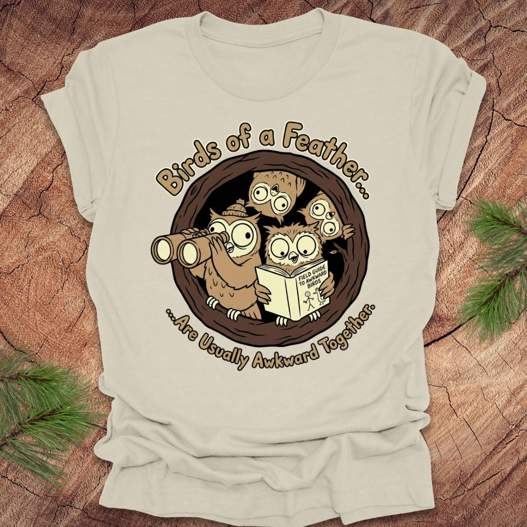 Beige t-shirt with owl graphic and text on a wooden surface