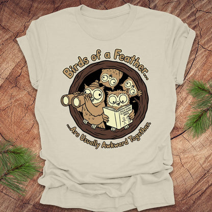 Beige t-shirt with owl graphic and text on a wooden surface