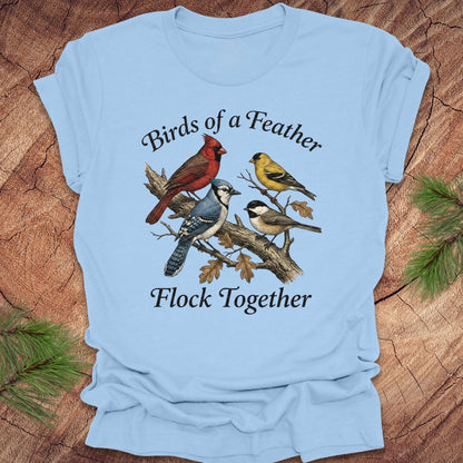 Light blue t-shirt with bird illustration and text on a wooden surface