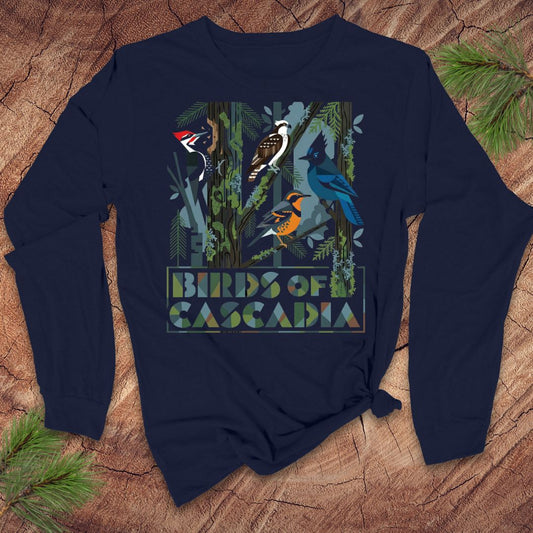 Navy blue long-sleeve tshirt with 'Birds of Cascadia' design on a wooden surface with pine branches.