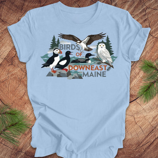 Light blue t-shirt with birds of downeast maine graphics and text on a wooden surface