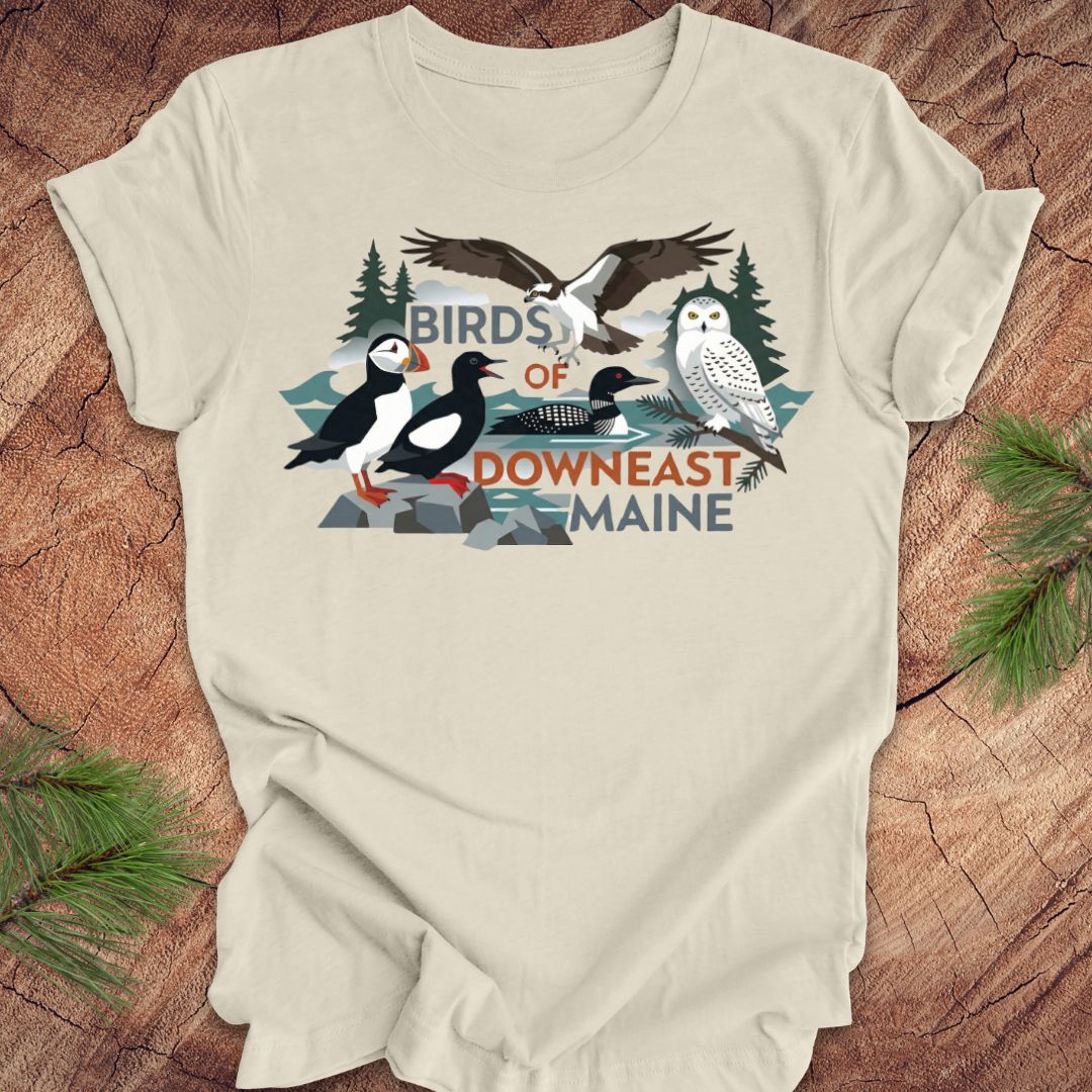 Beige t-shirt with birds of downeast maine graphics and text on a wooden surface