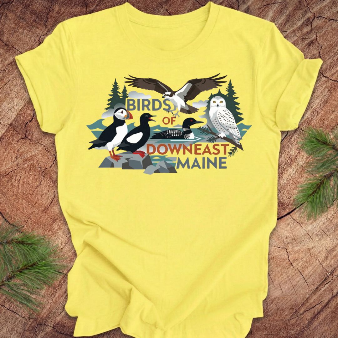 Yellow t-shirt with birds of downeast maine graphics and text on a wooden surface