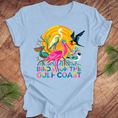 Blue t-shirt with bird design and text, 'birds of the gulf coast' on a wooden background.