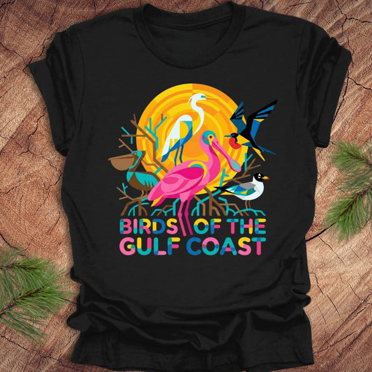 Black t-shirt with colorful 'Birds of the Gulf Coast' design featuring birds and a sunset on a wooden surface.