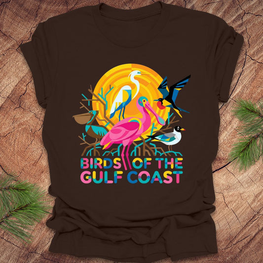 Brown t-shirt with colorful 'Birds of the Gulf Coast' design on a wooden surface