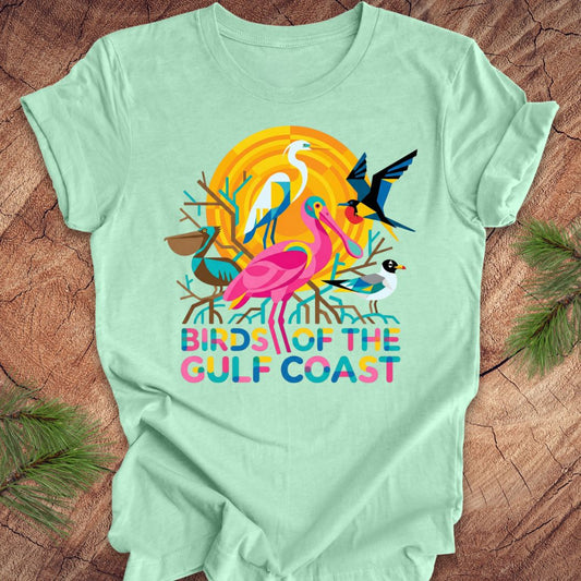 Mint green t-shirt with bird design and text, 'birds of the gulf coast' on a wooden background.