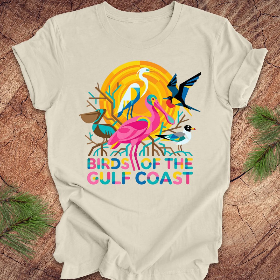 Beige t-shirt with bird design and text, 'birds of the gulf coast' on a wooden background.