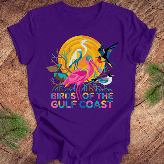 Purple t-shirt with bird design and text, 'birds of the gulf coast' on a wooden background.