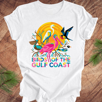 White t-shirt with bird design and text, 'birds of the gulf coast' on a wooden background.