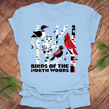 Light blue t-shirt with bird graphic and 'Birds of the North Woods' text on a wooden surface.