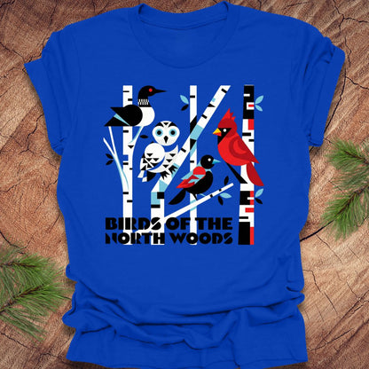 Royal blue t-shirt with bird graphic and 'Birds of the North Woods' text on a wooden surface.