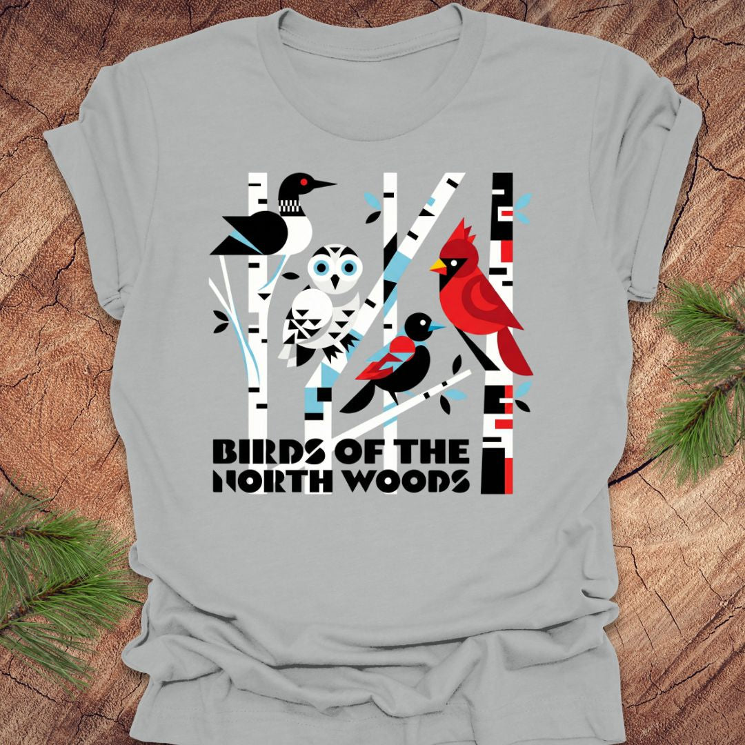 Gray t-shirt with bird design and 'Birds of the North Woods' text on a wooden surface.