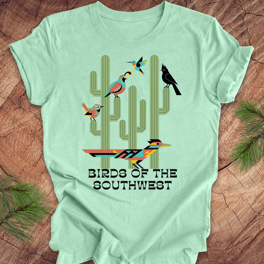 Mint green t-shirt with 'Birds of the Southwest' design featuring cacti and birds on a wooden surface.