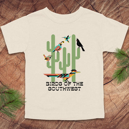 Beige toddler t-shirt with 'Birds of the Southwest' design featuring cacti and birds on a wooden surface.