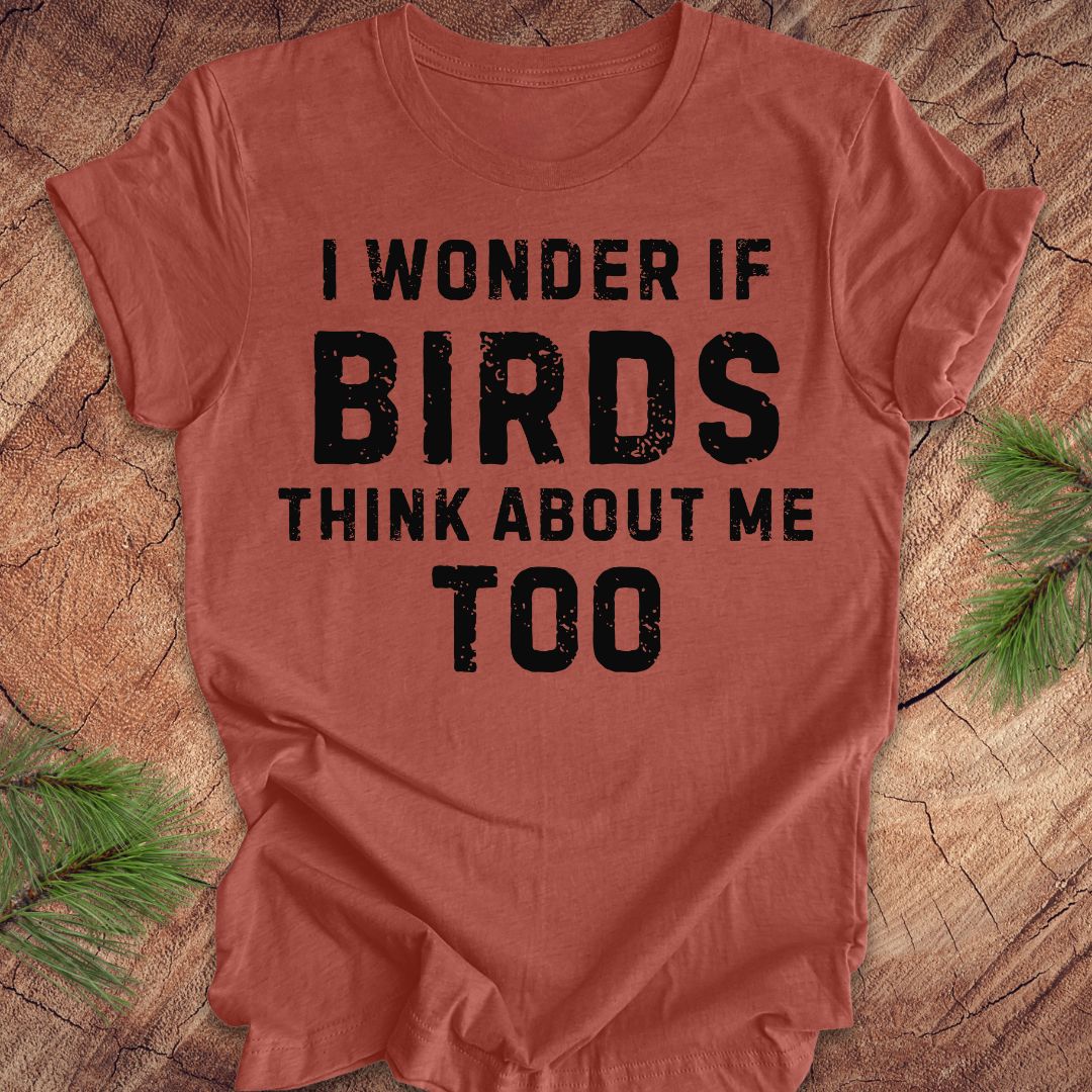 Red t-shirt with black text 'I wonder if birds think about me too' on a wooden surface.