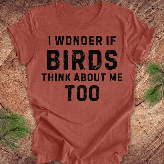 Red t-shirt with black text 'I wonder if birds think about me too' on a wooden surface.